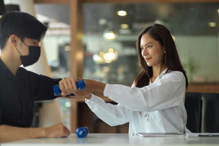 Attractive female therapist assisting male patient to do a physical therapy at health therapeutic centreの写真素材