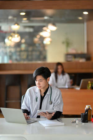 Young male intern doctor working on laptop, medical webinar, study medical case from medical online research in officeの写真素材
