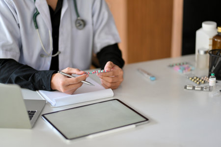A young male intern doctor or pharmacist sits at his desk, looking at his online medication history record on a digital tablet.の写真素材