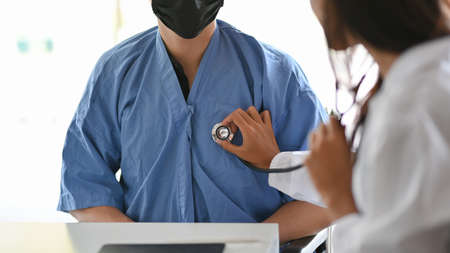 Female doctor using stethoscope to checkup male patient heartbeat in aid room at hospitalの写真素材