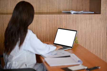 Female doctor or medical worker working on laptop computer, laptop blank screen mockup and medical report on wooden deskの写真素材