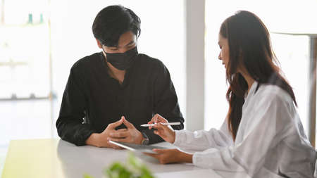 Male patient talking his sickness to female doctor at hospital, health checkup, disease treatmentの写真素材