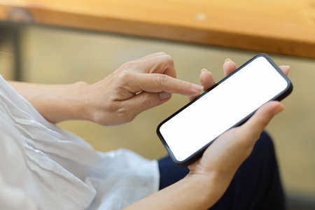 Close-up Senior woman in white shirt sitting on armchair, using mobile phone with blank screen...