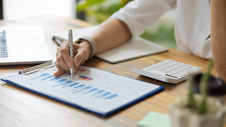 Close-up A businesswoman works on a financial chart report, calculates business costs and profits, and sits at her desk.の写真素材