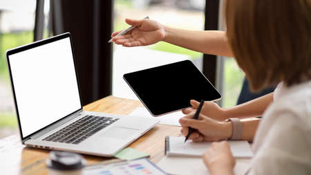 Two businesswomen meet in a meeting room for a business consultation, using a laptop computer and tablet. mockup of a laptop with a blank screenの写真素材