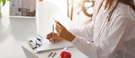 Close-up an Asian female doctor or pharmacist writes a medication prescription for a patient at the clinic. pack of pills, tablet blistersの写真素材