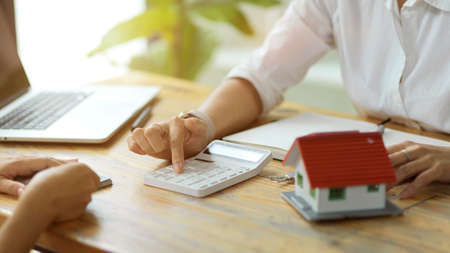 A female real estate agent estimates housing costs for a new client. On the table, there is a laptop and a house model.の写真素材