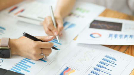Focus hands image, Two of businesswoman analysing financial graphs and charts, making notes on financial reportの写真素材