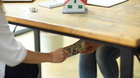 Corrupted businesspeople receiving a bribe money under wooden table, Real estate agent taking bribe...