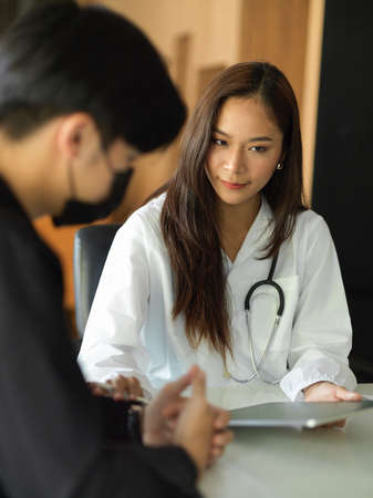 A serious young man patient consults with a female doctor about his diagnosis. The doctor explains medical information and the patient's diagnosis to the patient.の写真素材