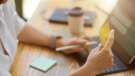 Close-up of an Asian woman holding a credit card while sitting at a workstation in front of a portable tablet. online banking, shopping, and e-commerceの写真素材
