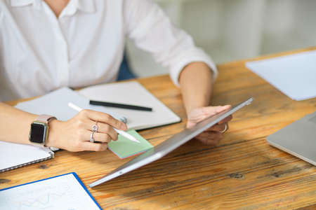 Cropped shot of female business worker working and managing business strategy plan on digital tablet sits at her deskの写真素材