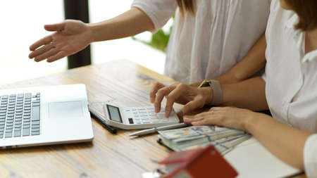 Cropped shot of Two woman talking and separating monthly house expenses. laptop, calculator and banknotes on tableの写真素材