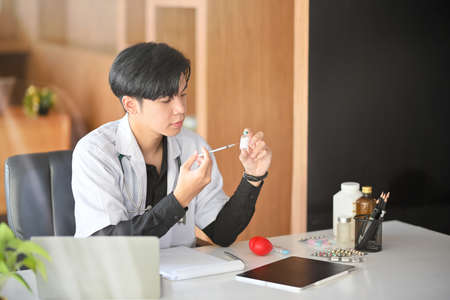 An Asian young male doctor extracts a vaccine from a vaccine vial with a clinical syringeの写真素材
