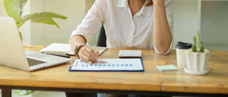 Cropped image of a senior businesswoman or female executive working at her desk in a modern office room, managing business data on a clipboard.の写真素材