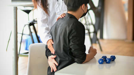 A male patient arrives at the therapy clinic complaining of low back pain. The therapist examines the patient's physical pain in examination roomの写真素材