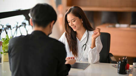 Cheerful asian female doctor discusses the medical treatment plan with male patient in examination room. Male patient make a follow-up appointment with a female physician.の写真素材