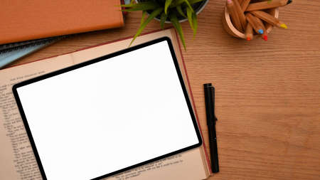 Top view, overhead view of study table with tablet computer blank screen mockup over a book with stationery on wooden tableの写真素材