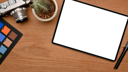 Closeup workspace with tablet blank screen mockup, colour checker and camera on wooden table. top view, overhead viewの写真素材