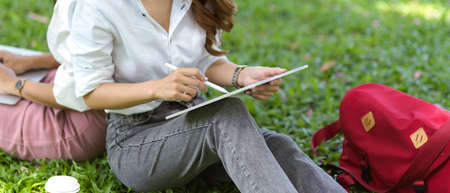 Female graphic designer college students in a park draw a landscape view on a digital graphic tablet...