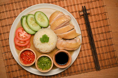 Top view, close-up of Hainanese chicken rice served with cucumber and tomato slides, chilli sauces and sweet soybean sauce. chopsticks on the table. Chinese styleの写真素材