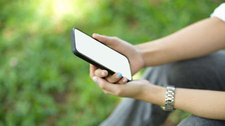 Side view, Female sits at a park and hold mobile phone. phone blank screen mockup for montage your...