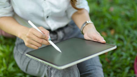 Cropped shot of Female using stylus pen to list an ideas or do digital graphic art work on tablet computer at parkの写真素材
