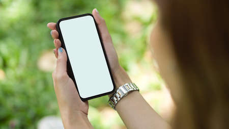 Close-up Young female holding smartphone. mobile phone blank screen for montage mockup with blurred green park background.の写真素材