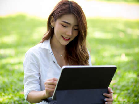 A cheerful female relaxes in a park and entertains herself with a portable tablet.の写真素材