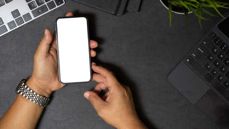 Top view of Male hands holding or using smartphone on working desk. Smartphone blank screen on black...