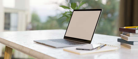 Simple home workspace with laptop computer blank screen mockup with supplies on a desk over blurred outdoor view in background. 3d rendering, 3d illustrationの写真素材