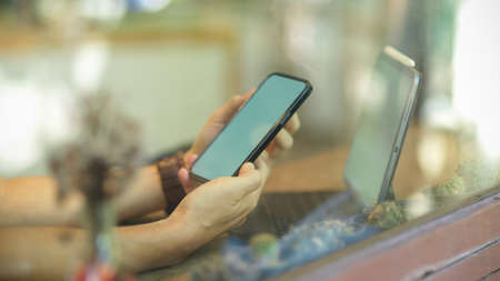 Close-up hands of business man holding smartphone and working on digital tablet in a coffee shop. mobile phone blank screenの写真素材