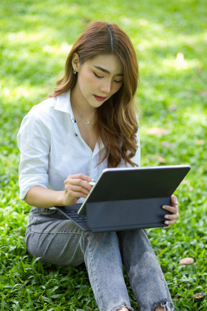 Charming asian female sitting at the yard using portable tablet. working outdoor and relaxingの写真素材