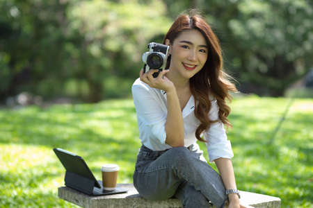 Attractive beautiful female sitting and relaxing in a park with retro cameraの写真素材