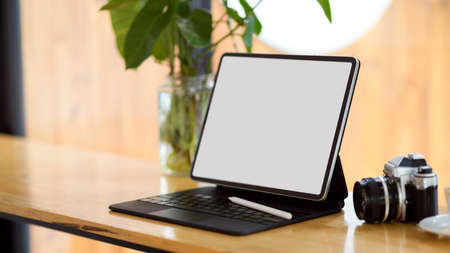 Portable tablet computer blank screen mockup for montage your graphic on screen stand on wooden table with retro cameraの写真素材