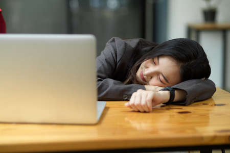 Tired or exhausted young business woman napping on working desk in front of her laptop in officeの写真素材