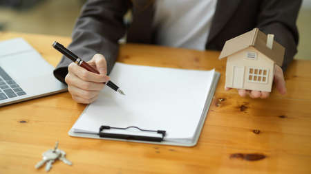 A female real estate agent drafts a rental agreement contract paper and holds a house model. cropped shotの写真素材