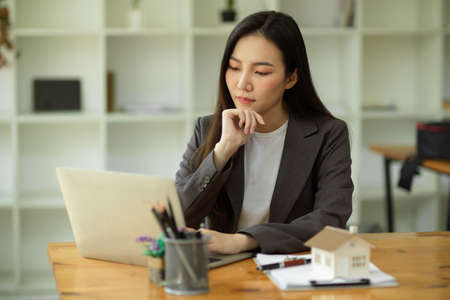 Serious businesswoman with hand on chin sitting and working on laptop computer, pensive thinking, pondering business strategy.の写真素材