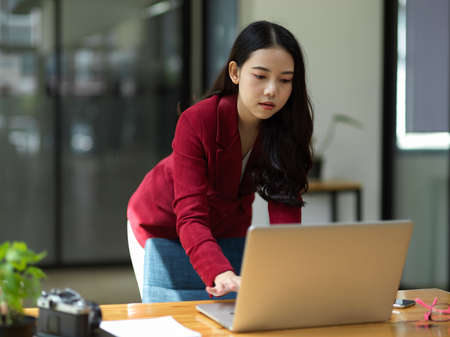 Elegance asian business woman working on laptop computer, leaning on worktable while looking down at laptop.の写真素材