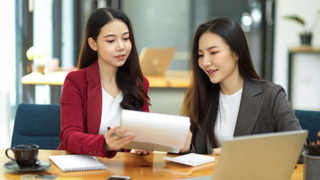 Two hardworking young smart business women working together on financial documents, reading the results in modern office.の写真素材