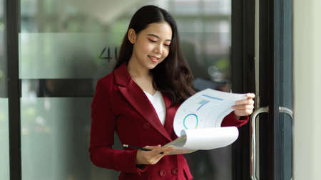 Satisfied business professional woman examines financial report papers, compares paperwork, or checks paper files.の写真素材