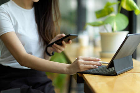 Cropped image of female working on portable digital tablet and smart mobile phone in co-working space. wireless technology conceptの写真素材