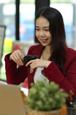 Portrait of a businesswoman holding a coffee cup while working on her laptop computer in a coffee shop.の写真素材
