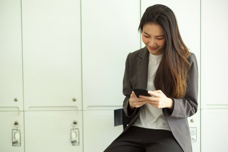 Attractive business woman in formal suit reading an email or texting message on smart mobile phone in a locker roomの写真素材