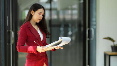 Young millennial asian female entrepreneur checking sale report papers on a clipboard, reading paperwork documents.の写真素材