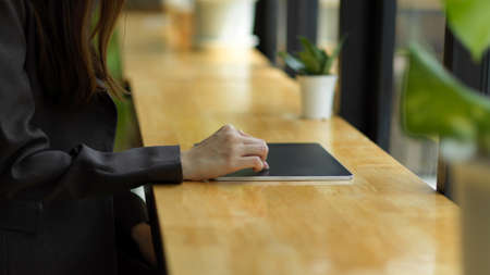 Cropped image of Business woman in black suit working on portable tablet on wooden table at cafeの写真素材