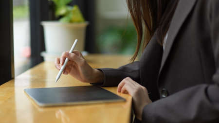 Cropped image of a beautiful businesswoman in a black suit taking notes on a digital tablet with a stylus pen.の写真素材