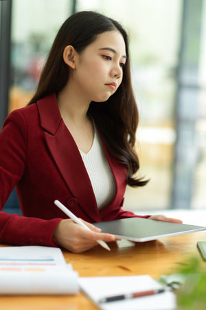 Unhappy young asian businesswoman working on tablet computer in the office, thoughtful, sad, worry about work result.の写真素材