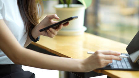Cropped image of millennial female college student sits in a coffee shop, working her assignment on portable tablet and smartphone.の写真素材