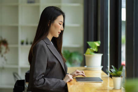 Successful and smart asian businesswoman in formal suit sits in the cafe on lunch break and working on her digital tablet computer.の写真素材